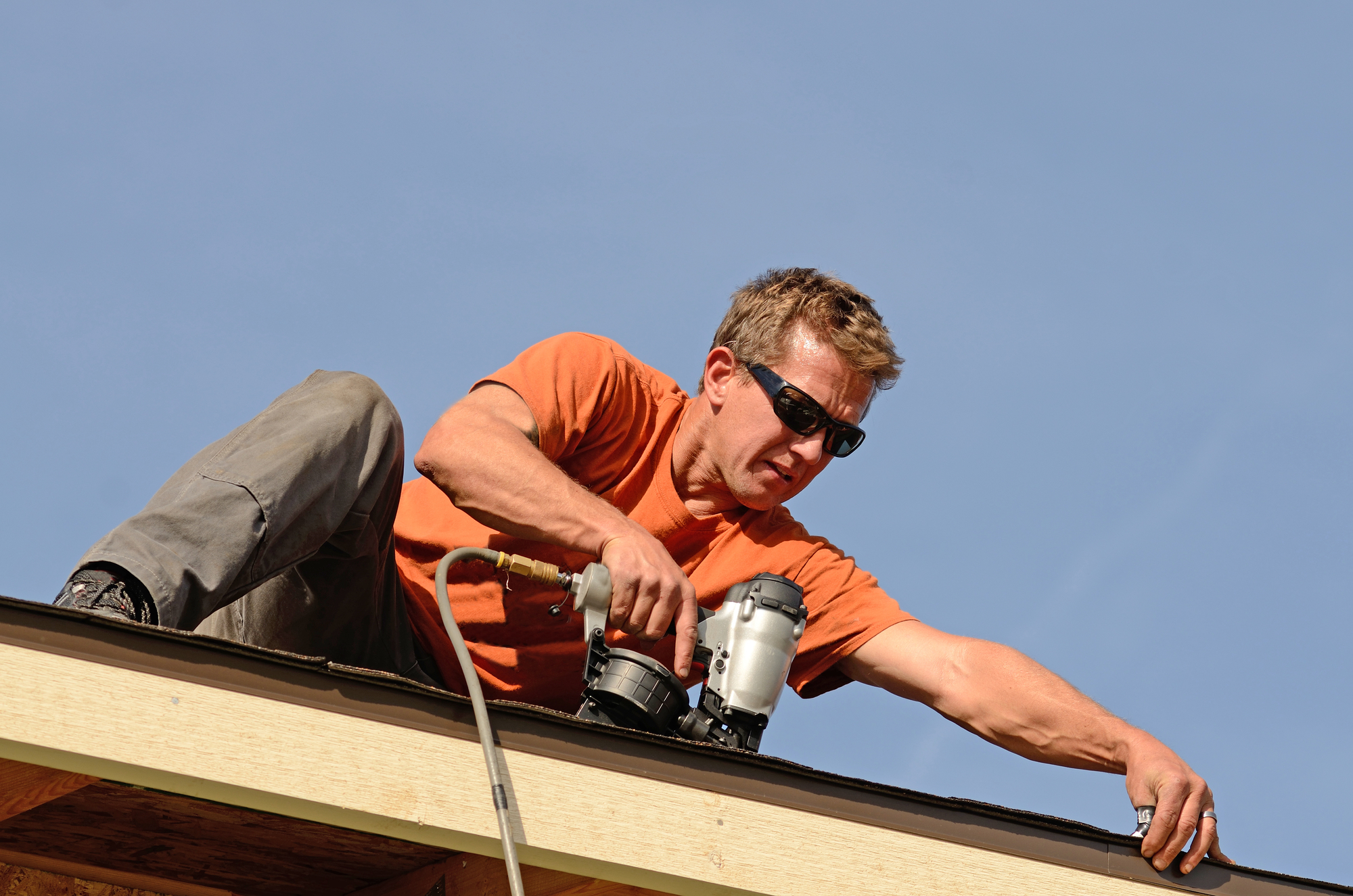 man with sunglasses uses nail gun to attach roofing